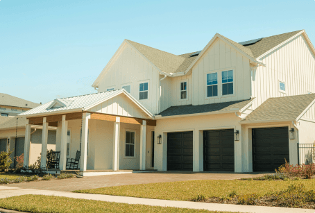 Maison moderne à deux étages avec façade blanche, toit en pente et trois portes de garage noires, entourée d'un jardin bien entretenu.