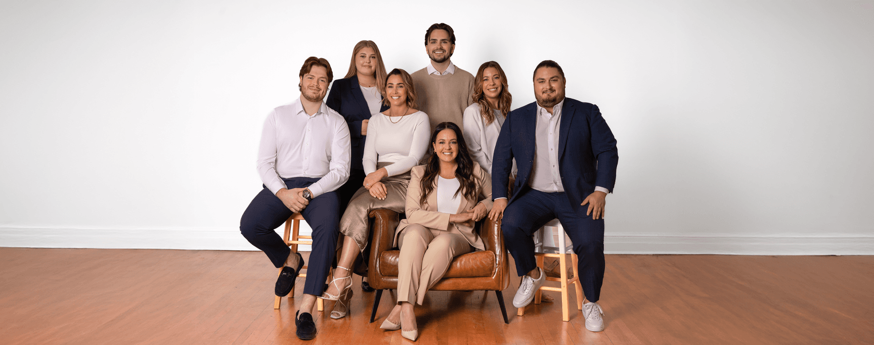 Groupe de sept personnes en tenue professionnelle décontractée, posant ensemble dans une pièce lumineuse autour d'un fauteuil en cuir