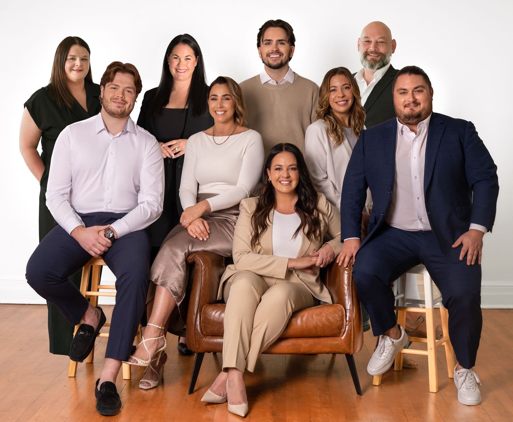 Groupe de neuf personnes souriantes posant dans un studio, habillées de tenues professionnelles dans des tons neutres, sur des chaises et un fauteuil en cuir.
